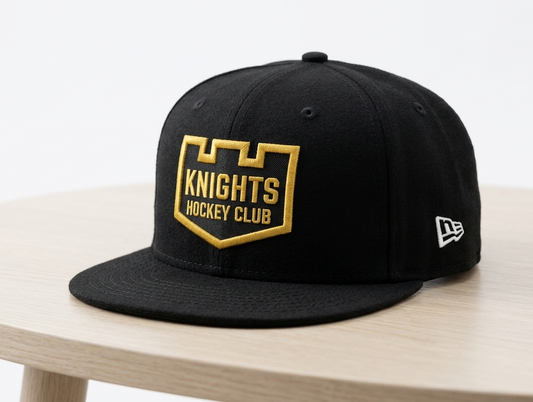 A black flat-brim New Era snapback cap featuring a gold and black Knights Hockey Club shield patch on the front, displayed on a light wood table against a white background.