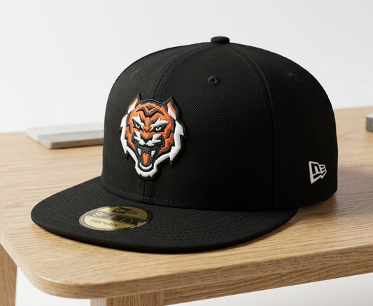 A black New Era 59FIFTY fitted cap featuring an embroidered red and white tiger head logo on the front, resting on a light wood table.